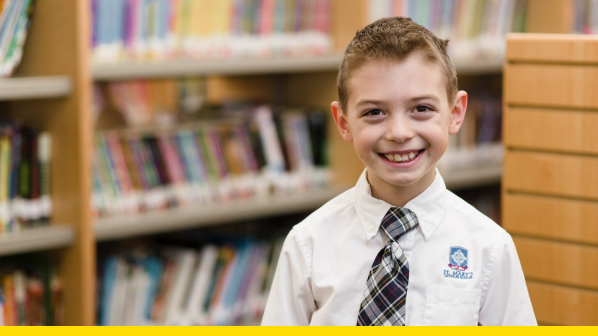 Young boy smiles while standing in the library in front of rows of books