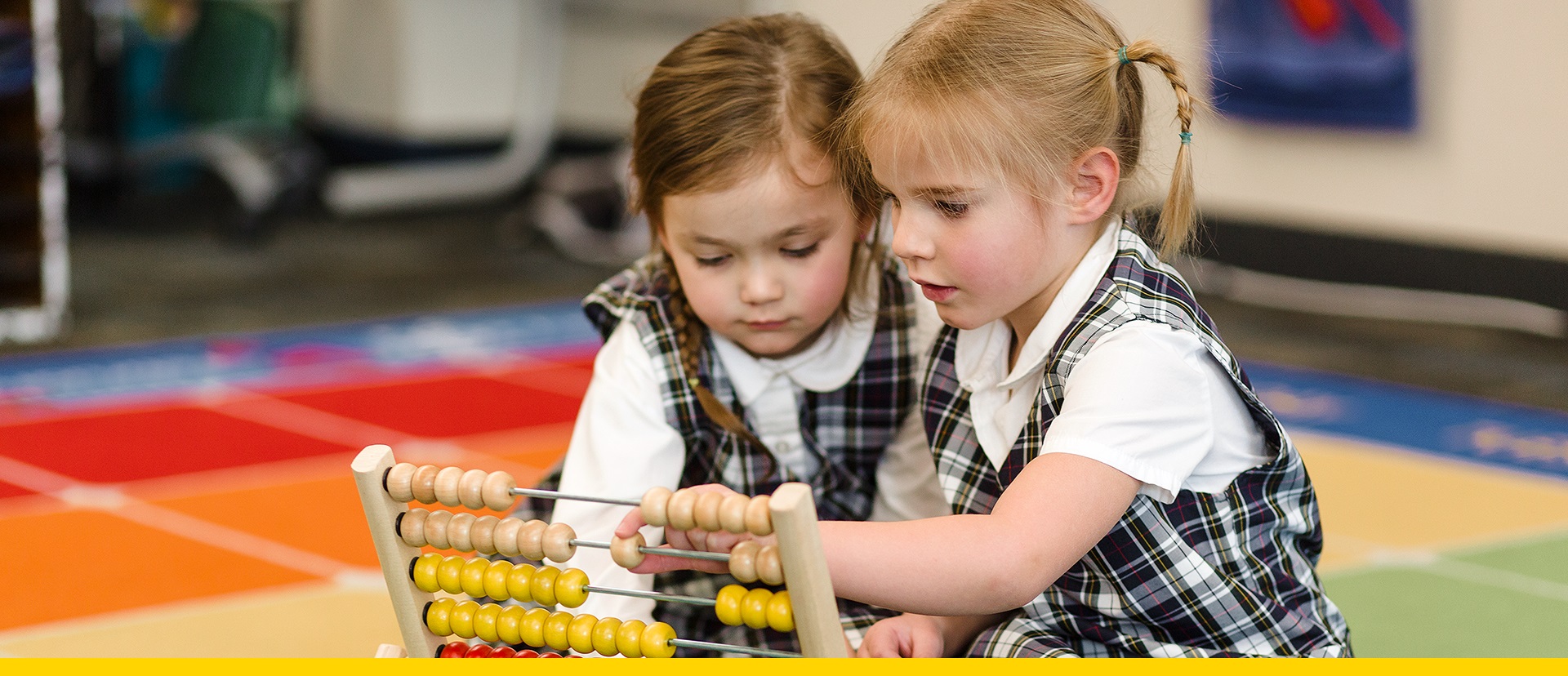 Two young girls sit on the floor of a classroom while working with an abacus