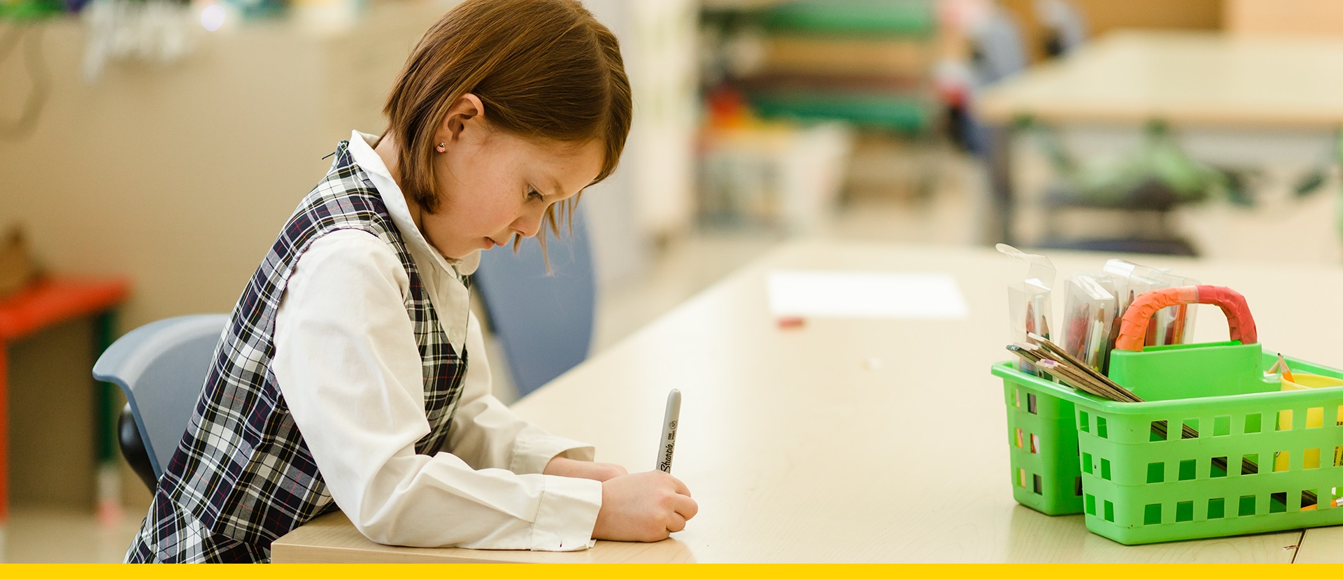 Young girl writing at a table in her classroom