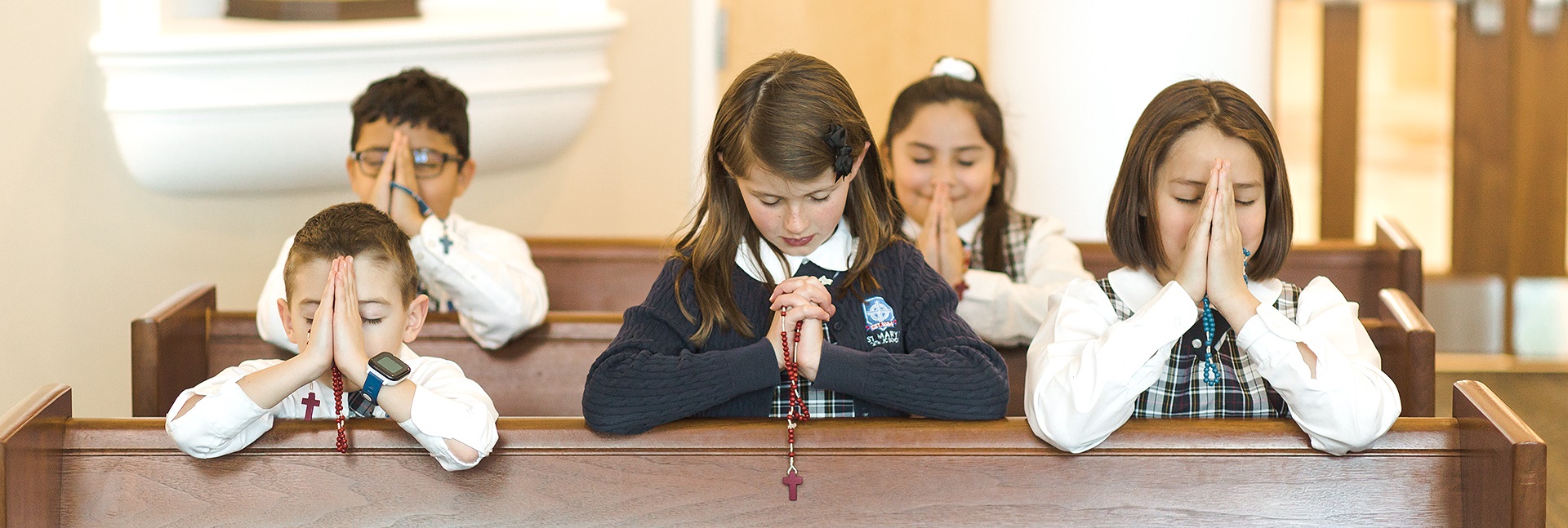 Diverse group of students praying in pews while wearing Catholic school uniforms