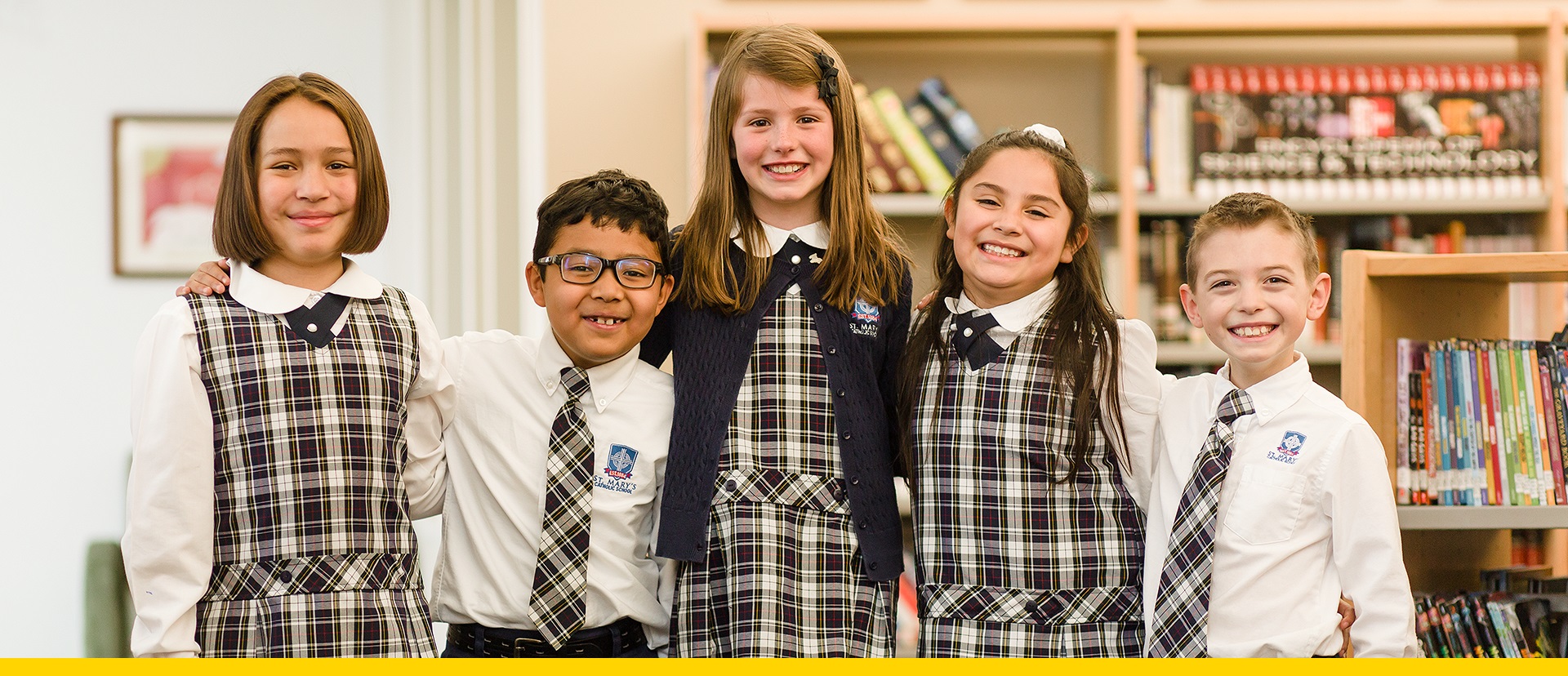 Diverse group of smiling students standing in the library while wearing St. Mary's Catholic School uniforms
