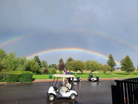 Double rainbow over golf course with golf carts in the forefront