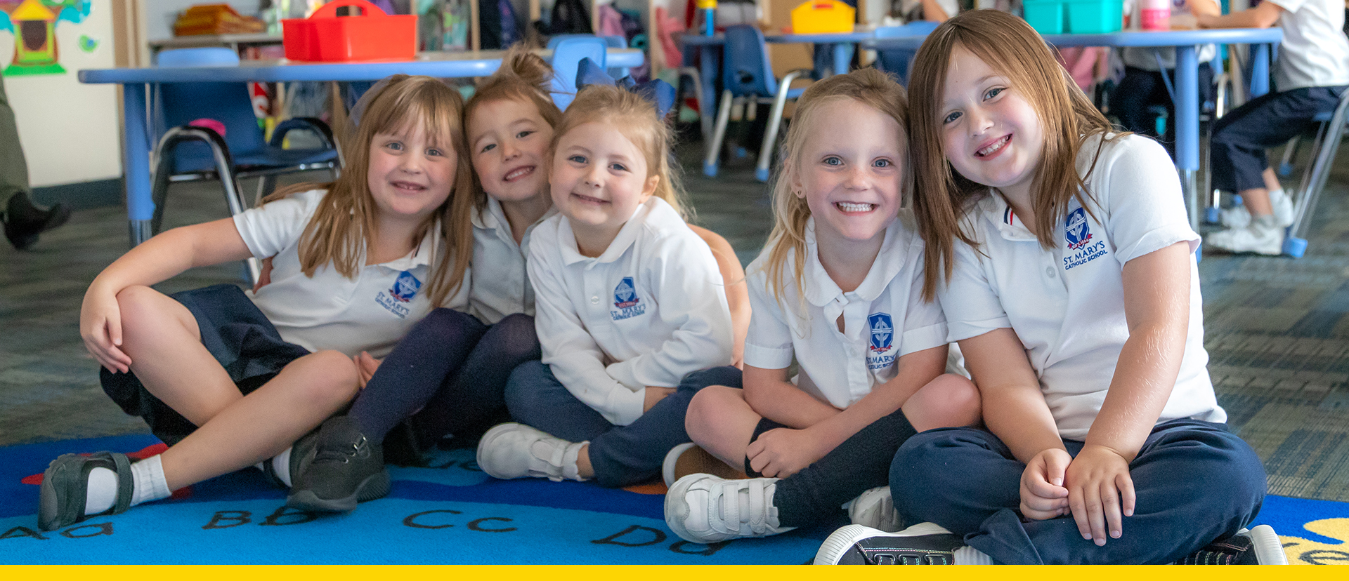 A group of kids sitting on the floor smiling at the camera