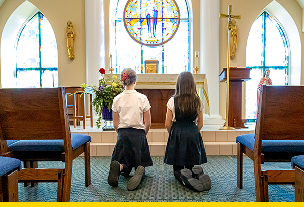 Two girls kneeling in a sanctuary praying
